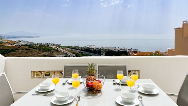 Una mesa lista para el desayuno con vista al mar y edificios al fondo.