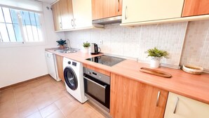 Una cocina compacta con armarios de madera, lavadora, horno empotrado y un lavabo.