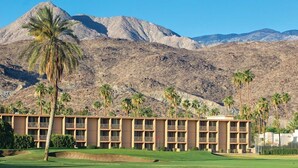 Een hotel met meerdere verdiepingen, een golfbaan op de voorgrond en bergen op de achtergrond.