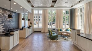 Ein geräumiger Raum mit Holzboden, einer Sitzecke mit Sofa und Sesseln, einer Theke mit einer Kreidetafel und großen Fenstern mit Vorhängen.