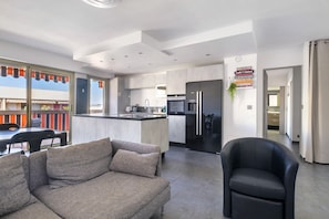 Une cuisine moderne dotée d’un îlot central, un coin repas avec une table et des chaises, et un espace de détente avec un canapé et un fauteuil.