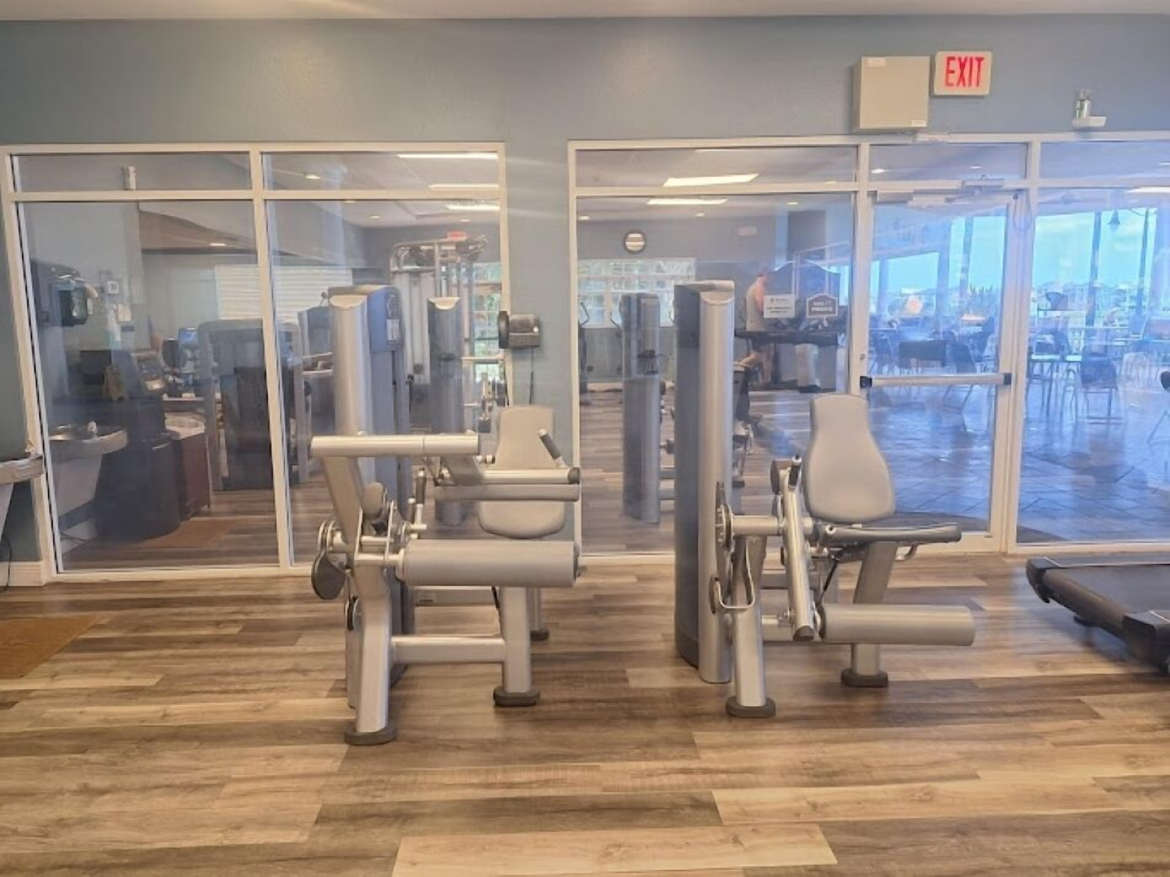 A gym with exercise equipment, large windows, and an exit sign.