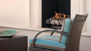 A patio area with a stone fireplace, a wicker chair with cushions, and a small table with a decorative item. - Reunion | Upscale Golf Retreat | Pool + Golf | 3BR Sleeps 8 (Reunion)