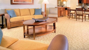 A living room with a sofa, a coffee table, a lamp, and a dining area with chairs and a table. - Reunion | Upscale Golf Retreat | Pool + Golf | 3BR Sleeps 8 (Reunion)