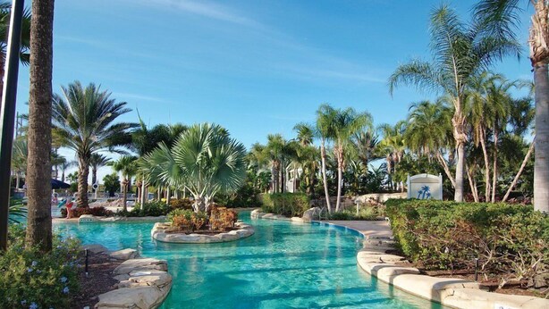 A swimming pool surrounded by palm trees and greenery, with a clear blue sky. - Reunion | Upscale Golf Retreat | Pool + Golf | 3BR Sleeps 8 (Reunion)