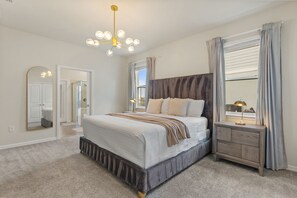 A bedroom with a large bed, a nightstand, a mirror, a chandelier, and a window with curtains. - 10 BD/ 8 BA/ Windsor Island Resort (2120 LC) (Davenport)