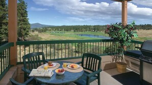 Un balcon avec une table préparée pour le petit-déjeuner, des chaises, un barbecue et une vue sur un lac et une forêt.