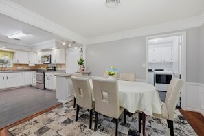 A modern kitchen with white cabinetry, a dining area with a table and chairs, and a visible laundry machine. - WinStar Getaway: 3 bedroom 2 full bath - Sleeps 6-10 - Lot of Parking - EV Port (Gainesville)