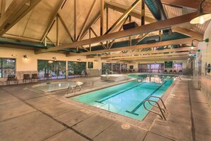 An indoor swimming pool with a high ceiling, built-in seating, and large windows.