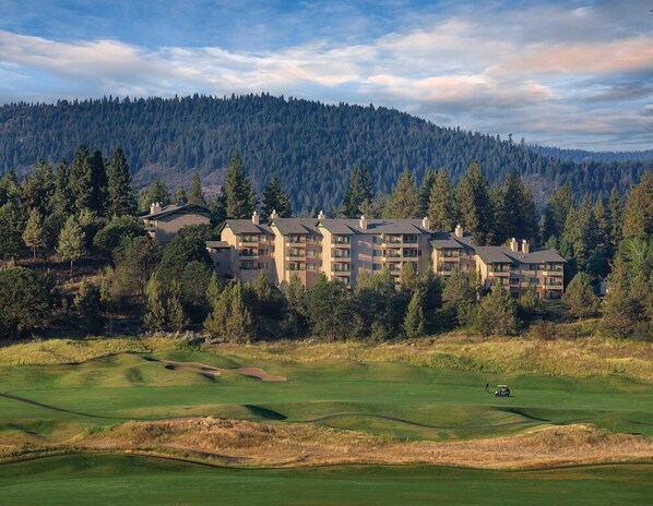 A multi-story hotel with a flat roof, surrounded by a golf course and dense forest.