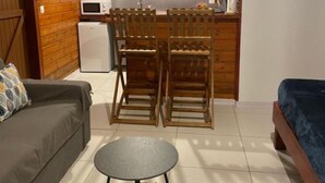 Un espacio habitable compacto con kitchenette, una zona de comedor con sillas de madera, un sofá y una pequeña mesa redonda.