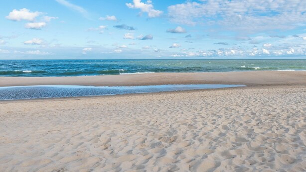 En sandstrand med milda vågor och en klar himmel.