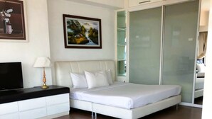 Un dormitorio con cama, televisor, lámpara, un cuadro y armario.