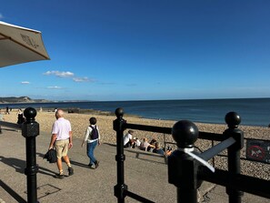 A coastal walkway with a clear view of the sea, a pebble beach, and a stone wall. - Smugglers Cottage Barn Conversion with Indoor Pool 
Jurassic Coast AONB (Whitchurch Canonicorum)
