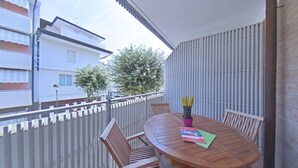 A balcony with a wooden table, chairs, and a potted plant. - Just Around the Corner From the Beach in Lignano (Lignano Sabbiadoro)