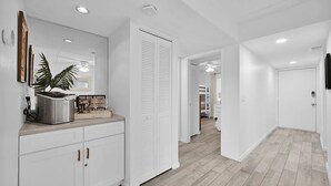 A modern hallway with white cabinetry, a kitchen area with a stainless steel appliance, and a ceiling fan. - Beachside Condo Resort Sleeps 6 in Beautiful St Augustine! (St. Augustine)