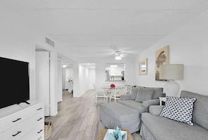Ein modernes Wohnzimmer mit Flachbildfernseher, grauem Sofa und einem Essbereich mit Glastisch.
