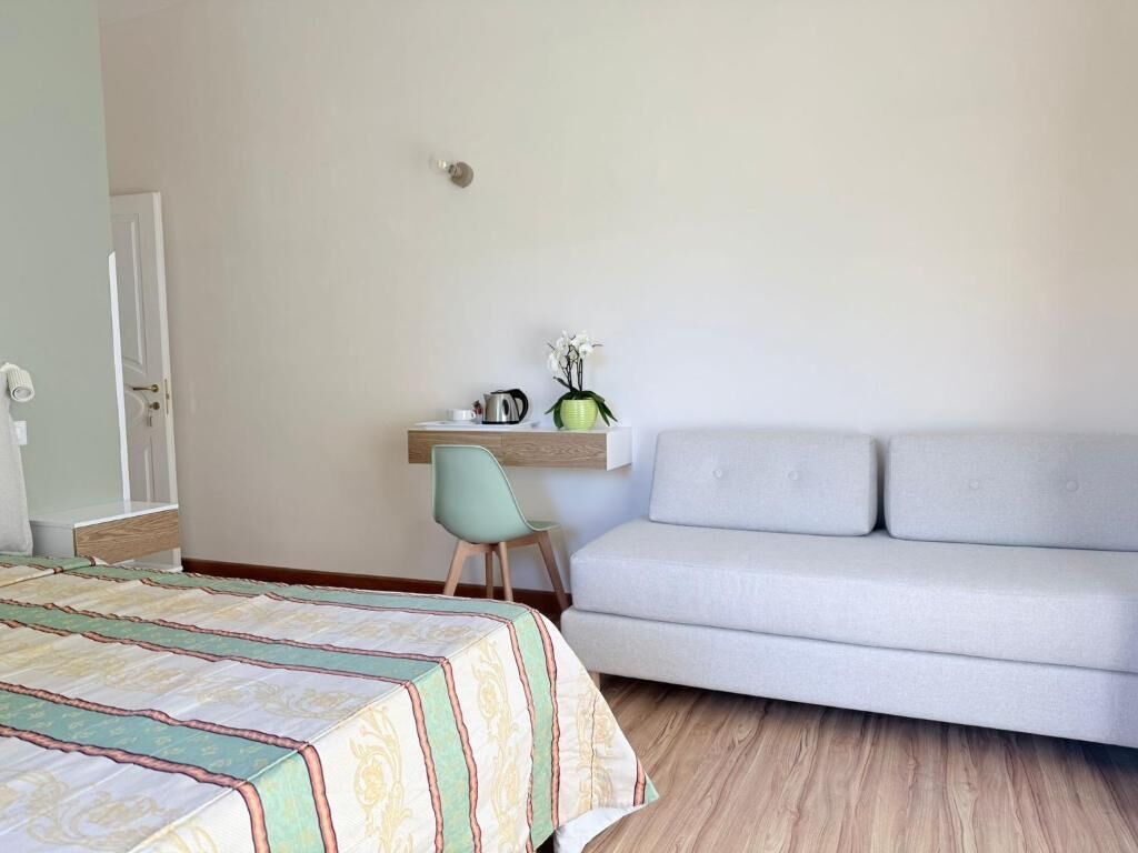 A bedroom with a bed, a desk, a chair, a sofa, and a wall-mounted shelf with a vase of flowers.