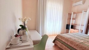 Een hotelkamer met een bed, een bureau met een stoel, een bijzettafeltje met een bloevas en een raam met gordijnen.