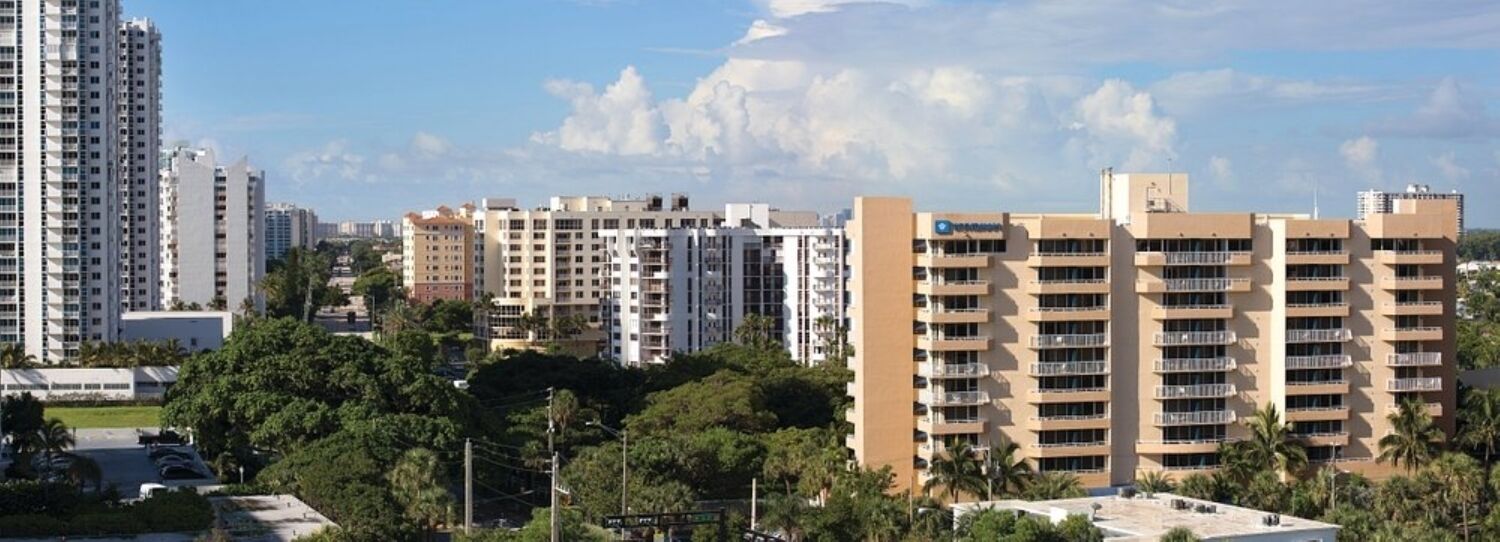 Un edificio alto con varios pisos, rodeado de vegetación y otros edificios.