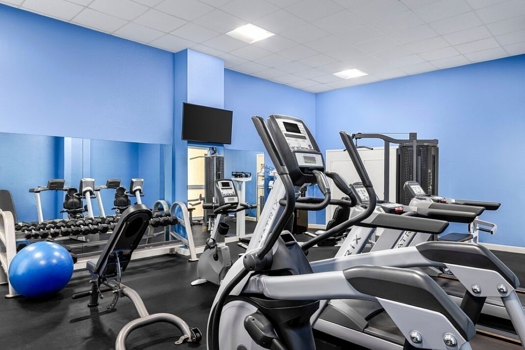 Une salle de sport équipée de matériel d’exercice, d’un téléviseur et d’un mur bleu.