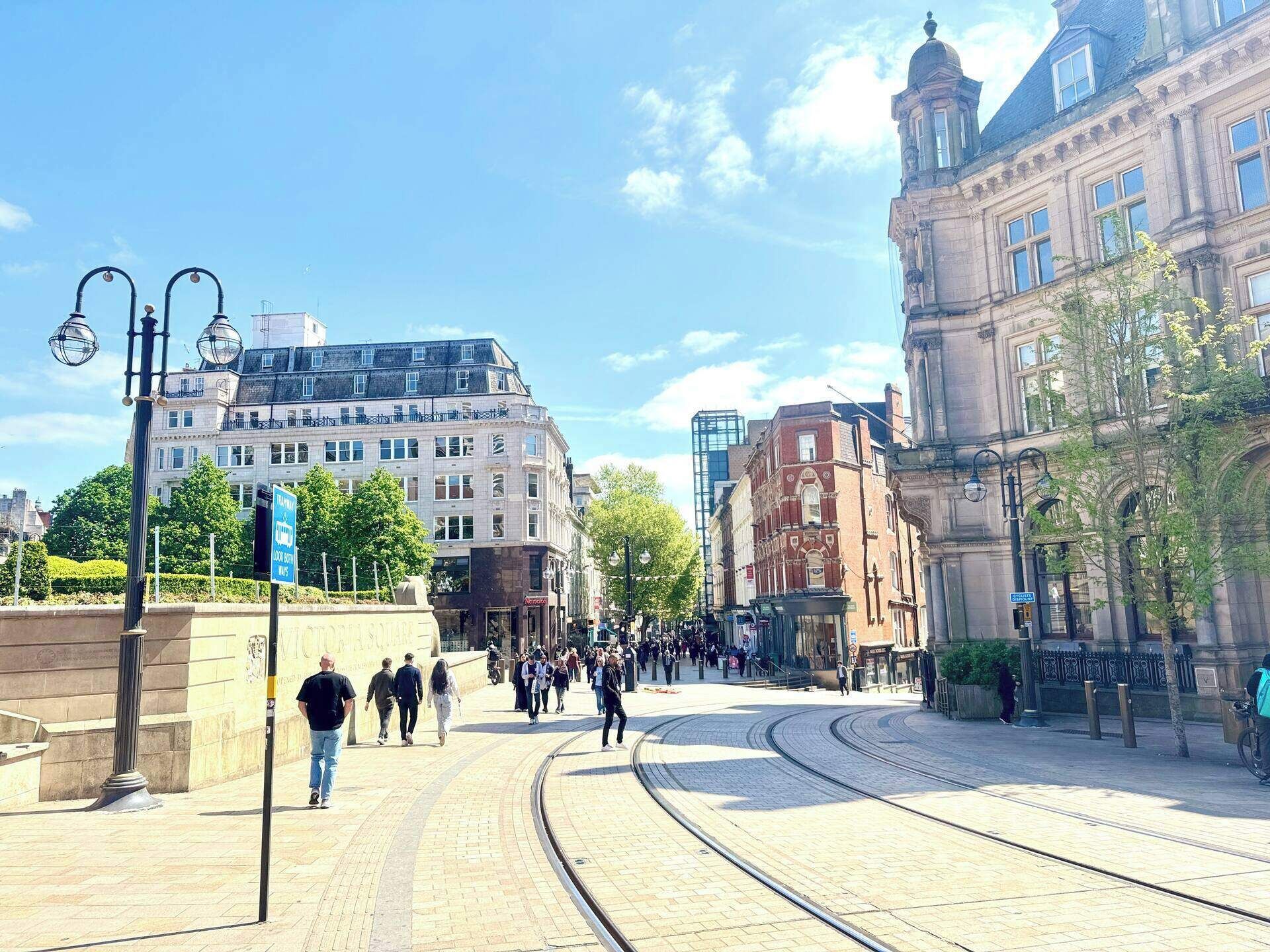 Een stadstraat met tramrails, historische gebouwen en voetgangers.