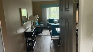 Un pasillo que conduce a un comedor con una mesa y sillas, un ventilador de techo y una ventana con cortinas.