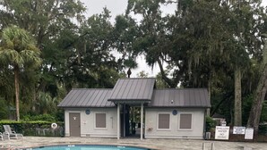 Piscina con puesto de socorrista, rodeada de árboles y una zona cubierta.