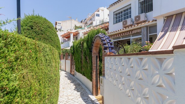 Un étroit sentier de pierre, bordé de haies soigneusement taillées et d’un mur blanc orné de motifs décoratifs.