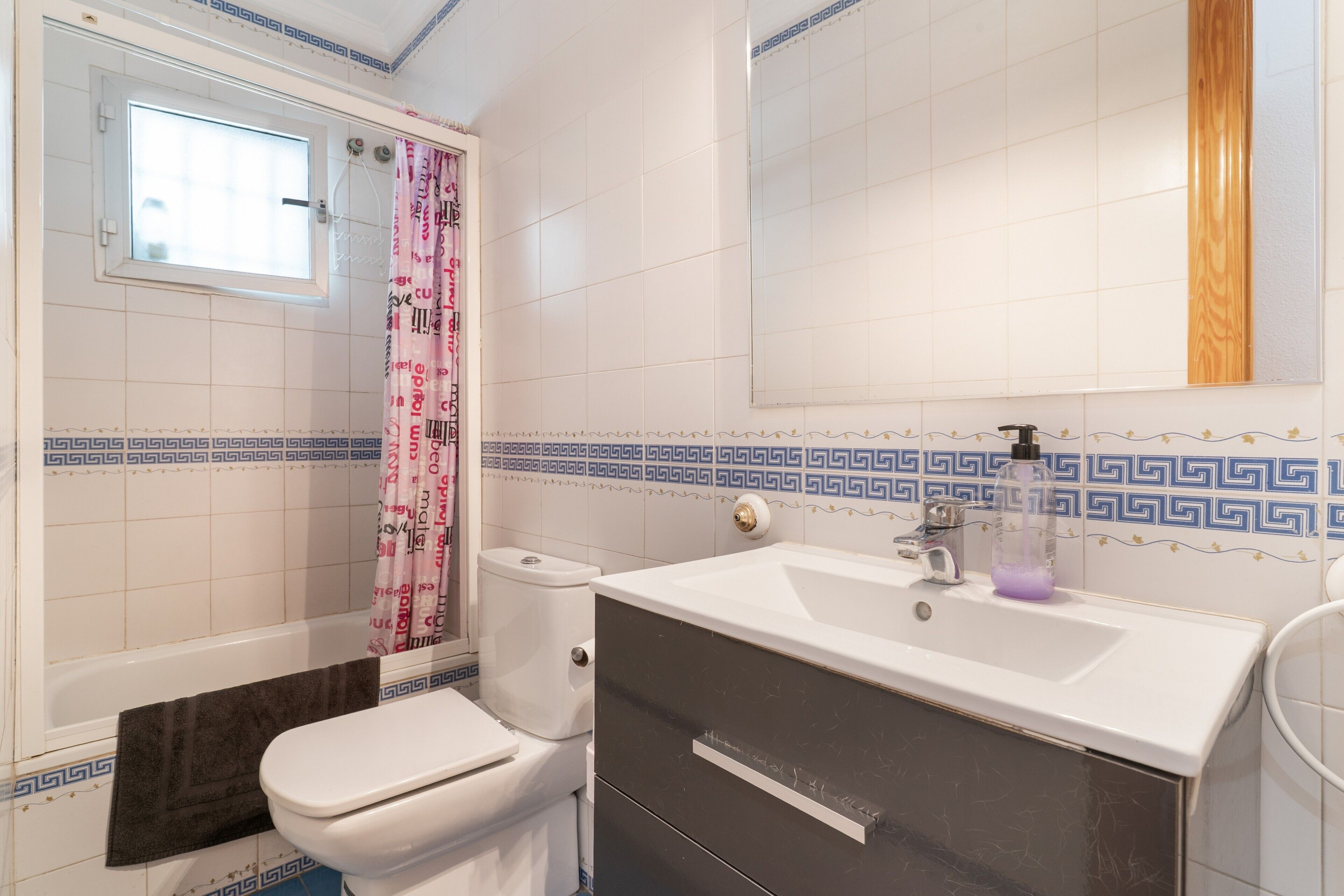 A bathroom with a toilet, a sink, a mirror, and a shower curtain.