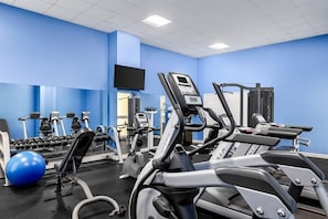 A gym with exercise equipment, a television, and a blue wall. - Santa Barbara | Romantic Beach Retreat | Pool + Beach (Pompano Beach)