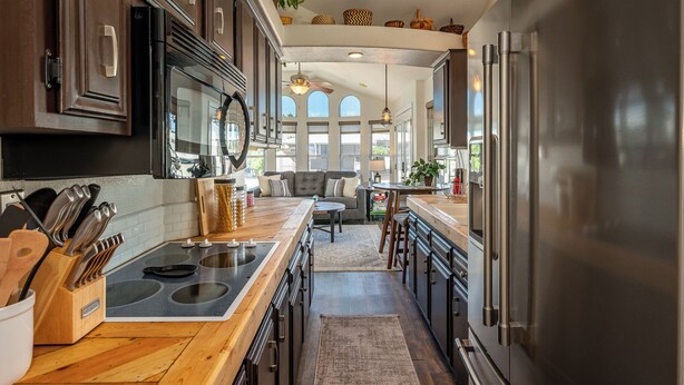 A kitchen with dark wooden cabinets, stainless steel appliances, and a central island with a sink. - Live on Island Time on Beachcomber Blvd, Lake Havasu City (Lake Havasu City)
