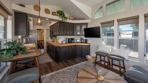 A modern kitchen with dark cabinets, a wooden island, and a dining area with a round table and chairs. - Live on Island Time on Beachcomber Blvd, Lake Havasu City (Lake Havasu City)