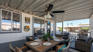 An outdoor covered patio with a dining table set for four, wicker furniture, a ceiling fan, and a view of the surrounding area. - Live on Island Time on Beachcomber Blvd, Lake Havasu City (Lake Havasu City)