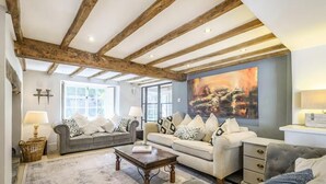 A spacious living room with exposed wooden beams, two sofas with patterned cushions, a coffee table, and a large abstract painting on the wall. - Cottage Sleeps 6 With Parking and Garden (Shipston on Stour)