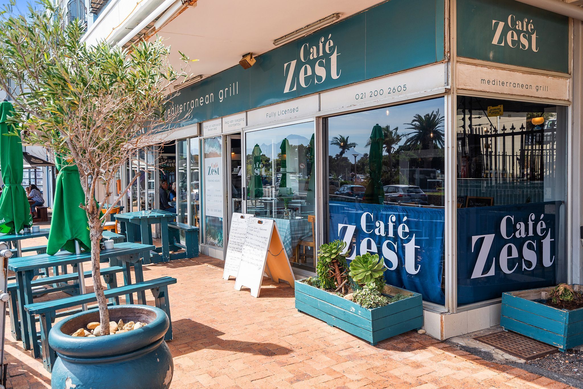 Un café avec une terrasse, une enseigne et un restaurant méditerranéen proposant un menu complet et disposant d’une licence pour servir des boissons alcoolisées.