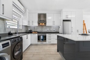 Eine moderne Küche mit weißen Schränken, einem eingebauten Backofen, einem Edelstahlkühlschrank und einer Waschmaschine.