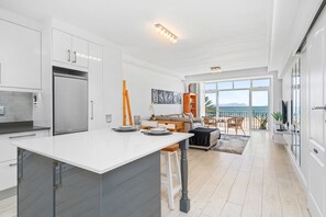 Eine moderne Küche mit einer großen Kochinsel, ein Essbereich mit Ausblick und ein Wohnbereich mit Sofa und Couchtisch.
