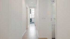 Un pasillo estrecho y bien iluminado, con paredes blancas y suelo de madera, que conduce a una habitación con ventana y puerta.