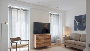 Una sala de estar moderna con una televisión de pantalla plana, un mueble de madera, dos sillas, un sofá y una lámpara.