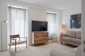 A modern living room with a flat-screen TV, wooden cabinet, two chairs, a sofa, and a lamp. - Master Deco Gem Avenidas Novas I – GEM Residence (Lisbon)