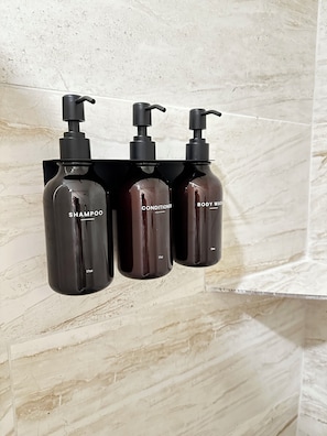 Three black bottles with pumps, labeled 'SHAMPOO,' 'CONDITIONER,' and 'BODY WASH,' hanging on a wall.