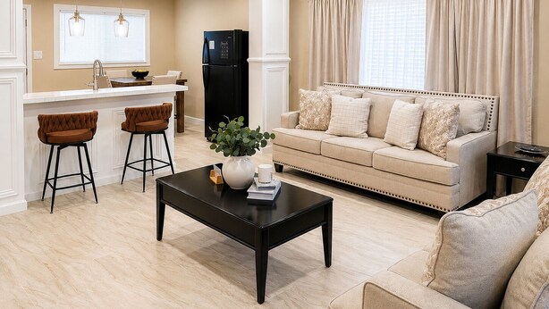 A modern living room with a sofa, two bar stools, a coffee table, and a kitchen area with a refrigerator.