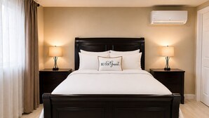 A hotel room with a dark wood bed, two bedside tables with lamps, beige walls, and an air conditioning unit.