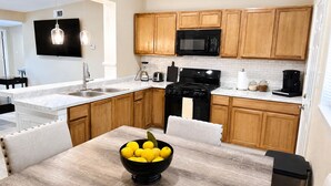 A modern kitchen with wooden cabinets, a black stove, a microwave, and a bowl of lemons on the table.