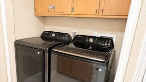 A laundry room with two front-loading washing machines and a dryer, wooden cabinets above, and a white tiled floor.