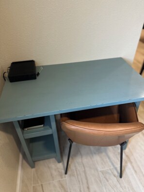 Un petit bureau bleu, avec une chaise en cuir, un appareil électronique noir posé dessus et un tiroir.