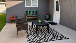 A patio with a table and chairs, a bench, potted plants, and a door.