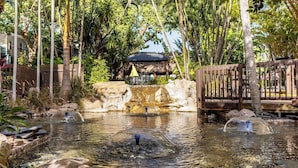 A tranquil outdoor setting with a pond, wooden deck, and a thatched-roof structure.