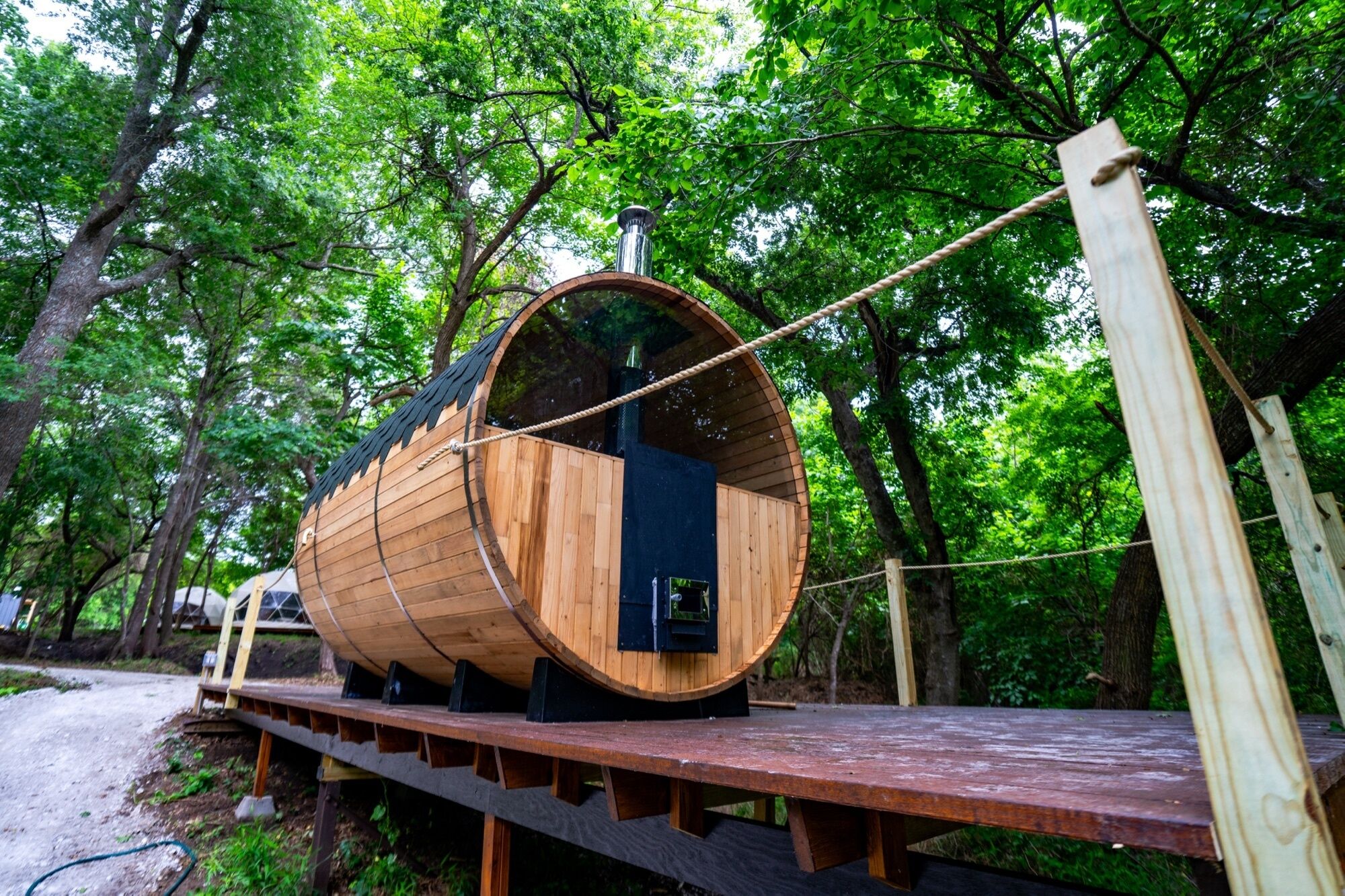 A wooden barrel-shaped structure with a small door, supported by a wooden platform, surrounded by trees.